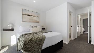 A modern bedroom with a large bed, a painting above the bed, and a hallway leading to other rooms.