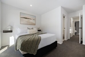 A modern bedroom with a large bed, a painting above the bed, and a hallway leading to other rooms. - Prime Location with mountain views (Queenstown)