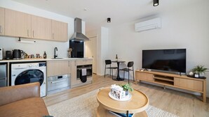Ett modernt kök med spis, ugn och tvättmaskin, en matplats med bord och stolar, en platt-TV och en mysig sittgrupp med ett soffbord.