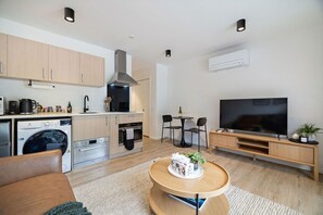 A modern kitchen with a stove, oven, and washing machine, a dining area with a table and chairs, a flat-screen TV, and a cozy seating area with a coffee table. - Lake and Mountain Views (Queenstown)