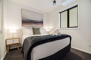 A hotel room with a bed, a bedside table with a lamp, a window, and a painting on the wall. - Lake and Mountain Views (Queenstown)
