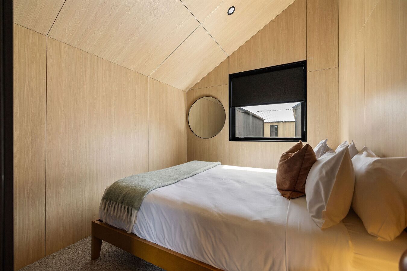 A bedroom with a bed, a round mirror, and a window.