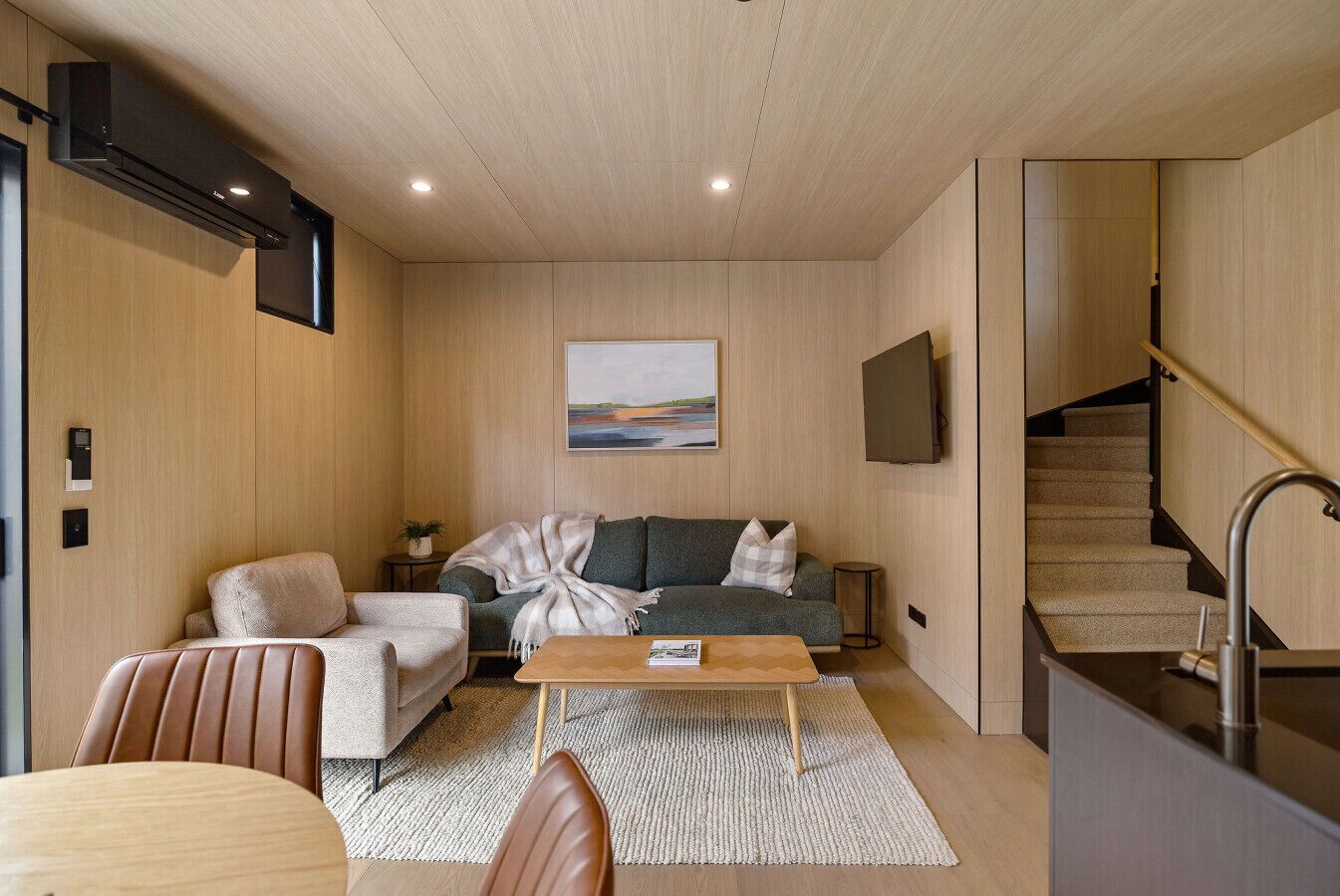 Een moderne woonkamer met een bank, fauteuil, salontafel en een schilderij aan de muur.