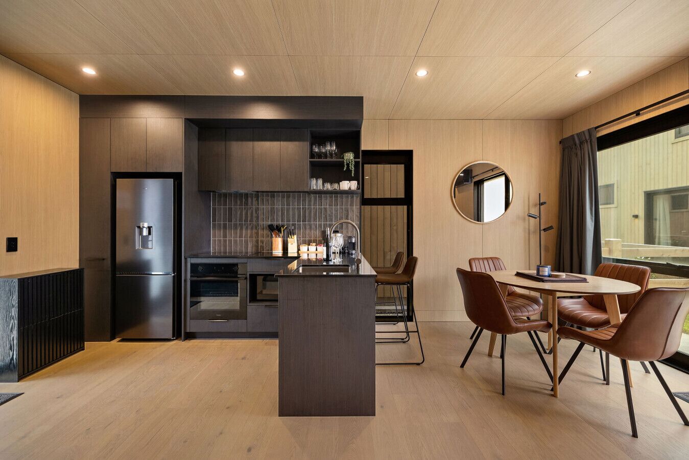 A modern kitchen with a central island, built-in appliances, and a dining area with leather chairs.