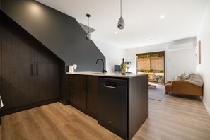 A modern kitchen with dark cabinetry, a dishwasher, and a dining area with a sofa and table. - Prime Location with mountain views (Queenstown)