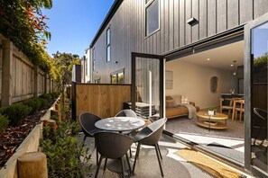 Ein modernes Haus mit Terrasse, Sitzgelegenheit im Freien und einer Glasschiebetür, die zu einem Wohnbereich führt.