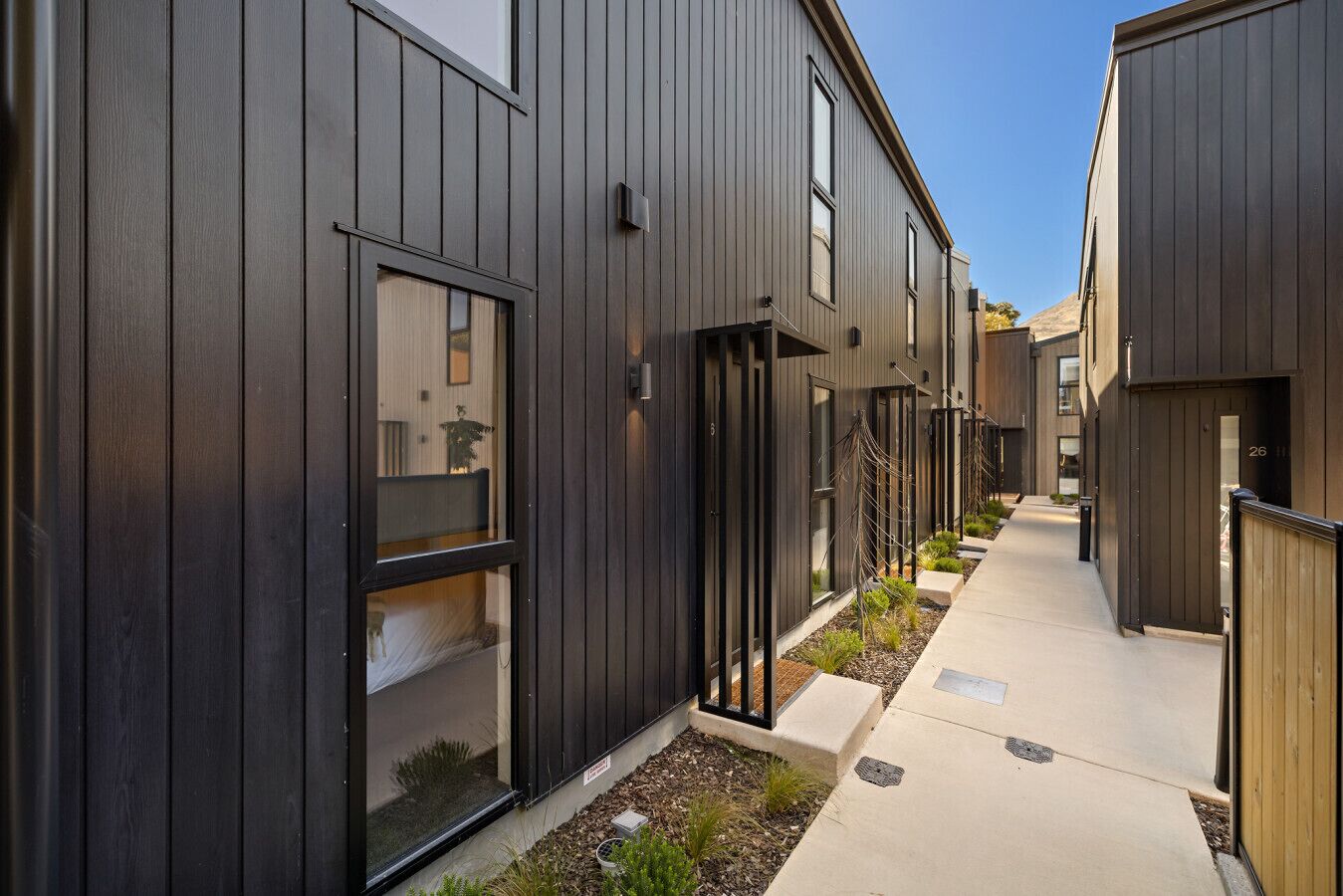 A modern building with dark wooden siding, large windows, and a narrow pathway.