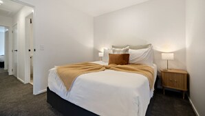 Una camera d'albergo con un letto grande, un comodino con una lampada e una porta che dà su un'altra stanza.