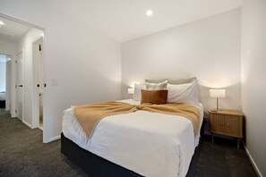 Ein Hotelzimmer mit einem großen Bett, einem Nachttisch mit Lampe und einer Tür zu einem weiteren Raum.
