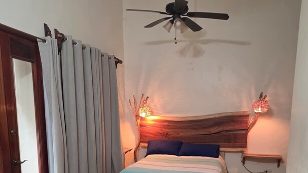 Ein Schlafzimmer mit Schachbrettfußboden, einem Bett mit blau-weiß gestreifter Bettdecke, einem Deckenventilator und zwei Wandleuchten.