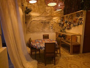 Uma sala de jantar com uma mesa redonda, cadeiras, uma prateleira fixada na parede com objetos decorativos e um chão estampado.