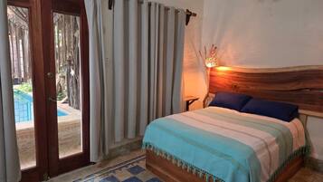 Une chambre à coucher avec un lit, des rideaux, une tête de lit en bois, une table de chevet et une vue sur une piscine extérieure.
