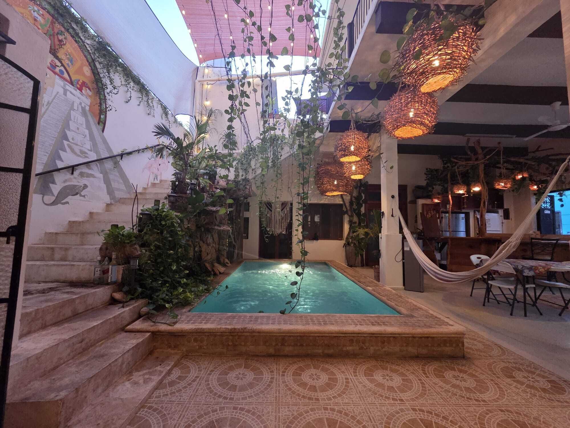 An indoor pool area with a tiled floor, surrounded by plants and a staircase.
