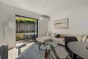 A modern living room with a glass door leading to a patio, a sofa, a coffee table, and a dining table. - Prime Location with mountain views (Queenstown)