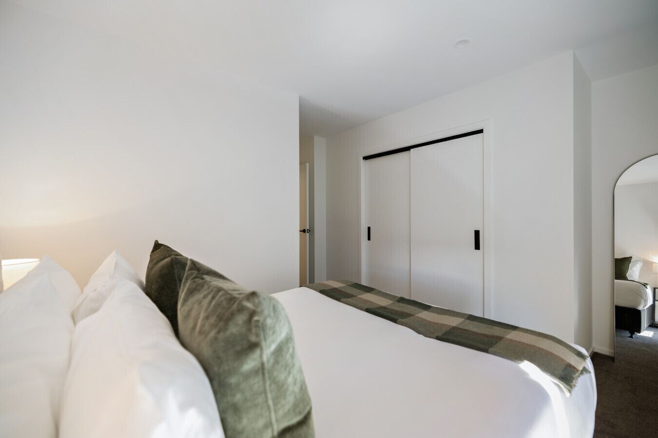 A hotel room with a bed, pillows, a checkered throw, a wardrobe, and a mirror.