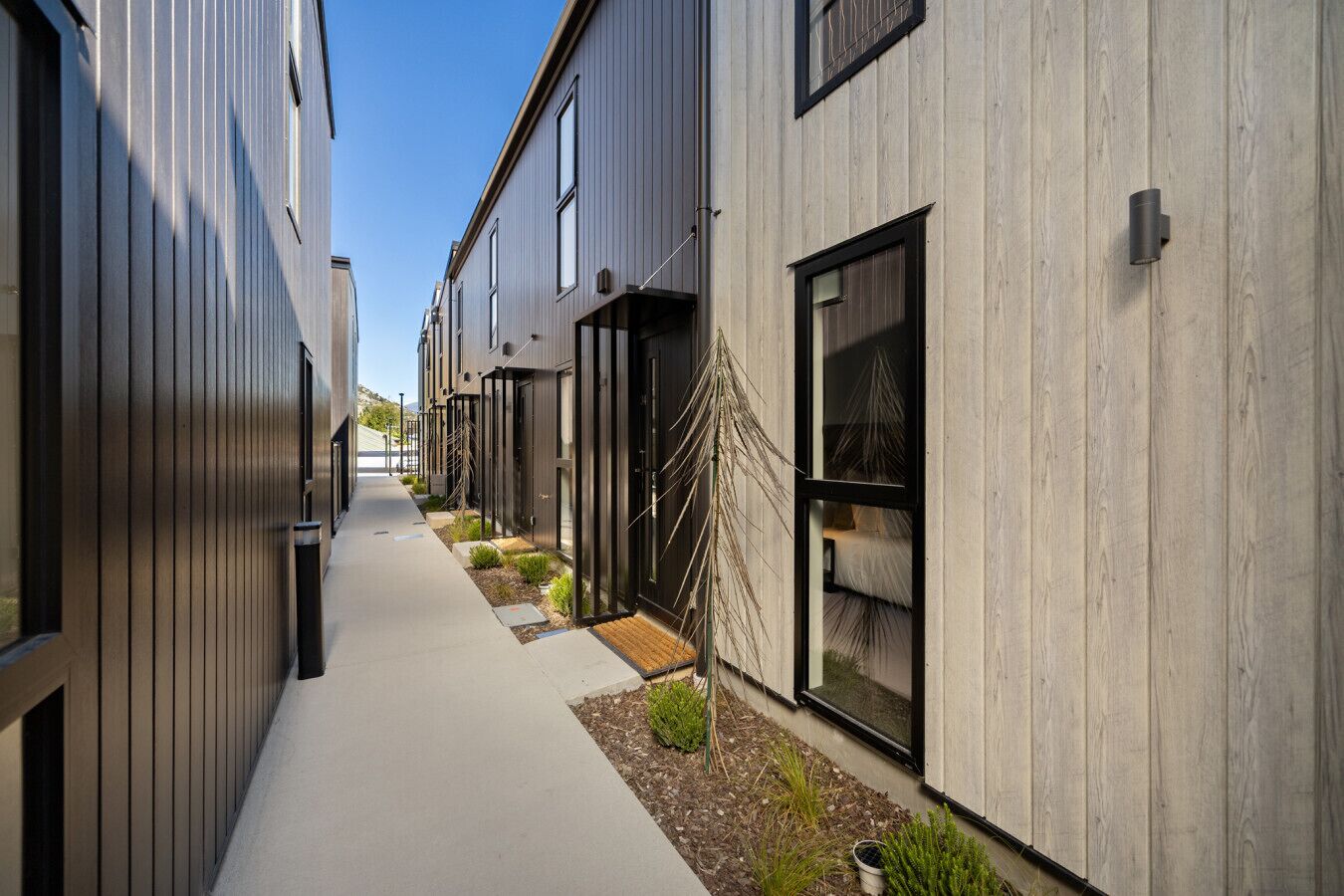 A narrow pathway between modern buildings with large windows and a small garden area.