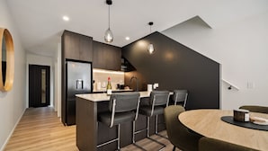 A modern kitchen with a central island, black bar stools, and a dining table with chairs. - Prime Location with mountain views (Queenstown)