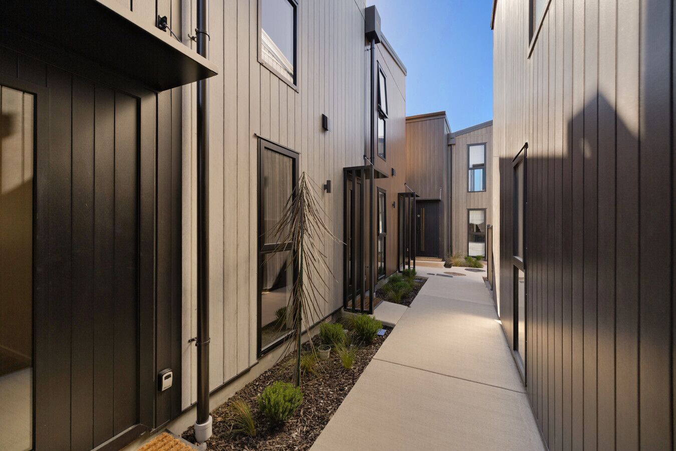A modern building with a narrow walkway, large windows, and a minimalist design.