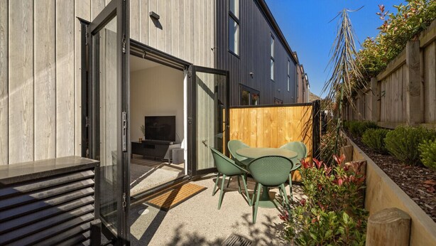 A modern house with a sliding glass door leading to a patio with a green chair and a small table. - Prime Location with mountain views (Queenstown)