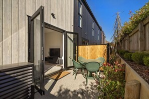 Ein modernes Haus mit einer Schiebetür, die auf eine Terrasse mit einem grünen Stuhl und einem kleinen Tisch führt.