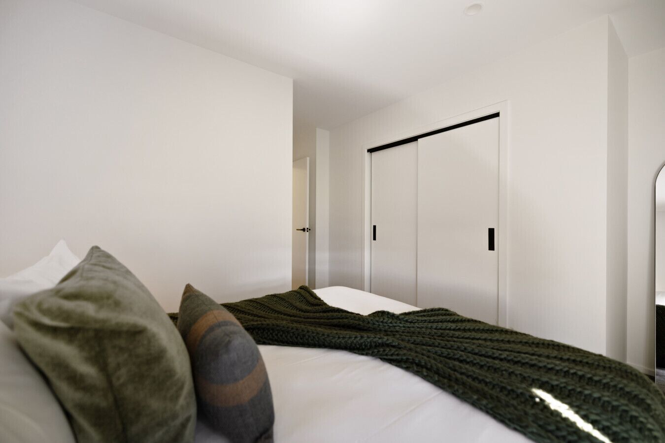 A modern bedroom with a bed, pillows, a knitted blanket, and a wardrobe with a black handle.