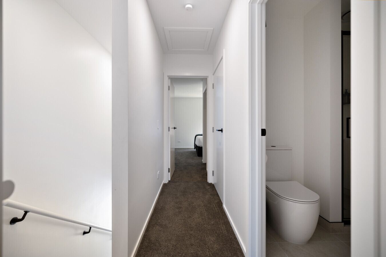 A hallway with white walls, a carpeted floor, and a toilet on the right.