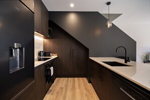 A modern kitchen with dark cabinetry, a wooden floor, a built-in oven, and a sink with a black faucet. - Prime Location with mountain views (Queenstown)