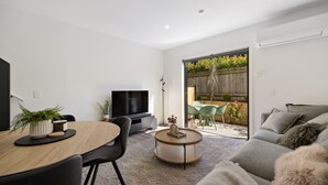 A modern living room with a flat-screen TV, a dining table with chairs, a sofa, and a small coffee table. - Prime Location with mountain views (Queenstown)