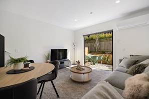 A modern living room with a flat-screen TV, a dining table with chairs, a sofa, and a small coffee table. - Prime Location with mountain views (Queenstown)