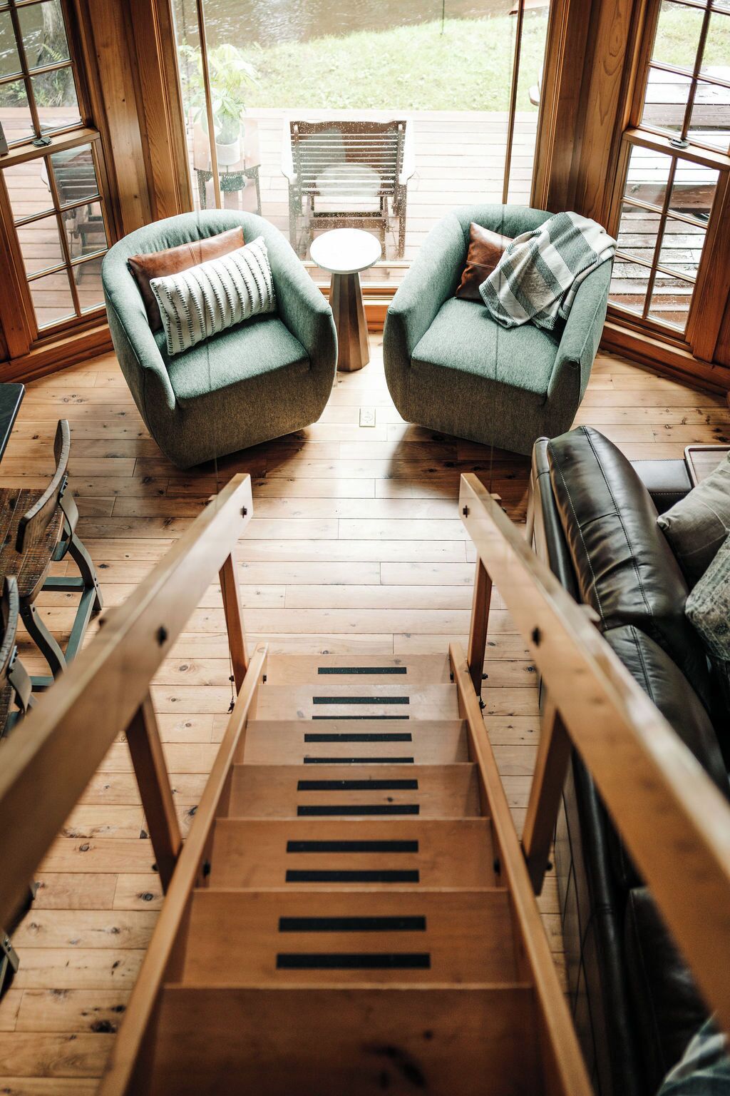Un escalier en bois mène à un espace détente comprenant deux fauteuils verts et un canapé en cuir noir.