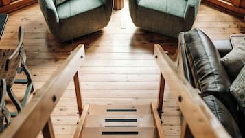 Un escalier en bois mène à un espace détente comprenant deux fauteuils verts et un canapé en cuir noir.