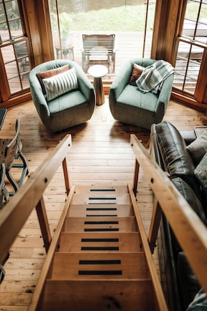 A wooden staircase leading to a seating area with two green armchairs and a black leather couch. - Magical Jordan River Oasis | Private Cabin & Deck (East Jordan)