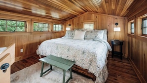 A wooden-paneled bedroom with a bed, bedside tables, and windows. - Magical Jordan River Oasis | Private Cabin & Deck (East Jordan)