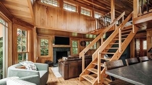 A spacious living area with a wooden staircase, a fireplace, and a dining table. - Magical Jordan River Oasis | Private Cabin & Deck (East Jordan)