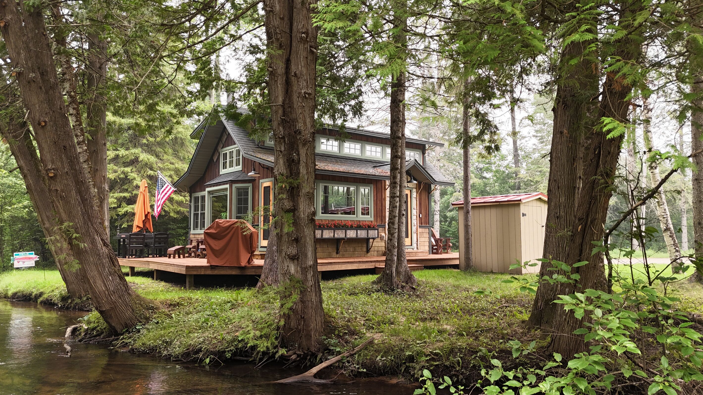 Une cabane avec une terrasse, un petit abri de jardin et un drapeau.