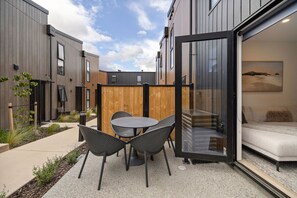 A modern outdoor patio with a table and chairs, a wooden fence, and a sliding glass door leading to an interior living space. - Prime Location with mountain views (Queenstown)