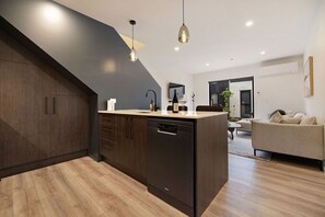 A modern kitchen with dark cabinetry, a dishwasher, and a countertop with a wine bottle and glasses. - Prime Location with mountain views (Queenstown)