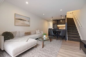 A modern living room with a sofa, coffee table, and a staircase leading to a kitchen. - Prime Location with mountain views (Queenstown)