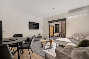 A modern living room with a dining area, a sofa, a coffee table, and a TV mounted on the wall. - Prime Location with mountain views (Queenstown)