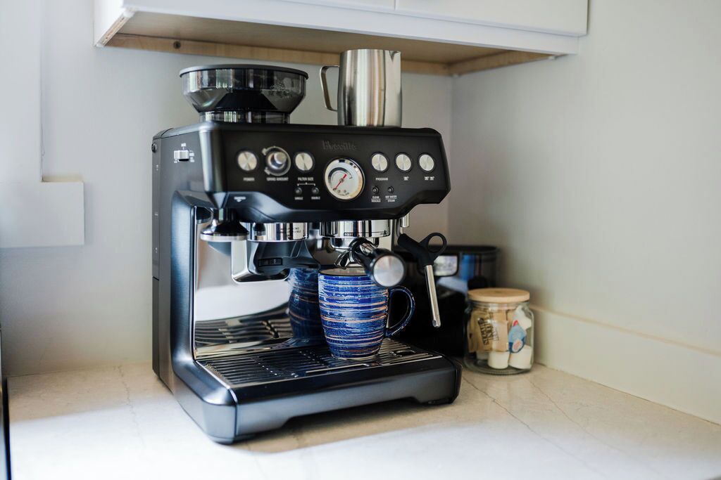 Une machine à expresso compacte dotée d’un écran numérique, d’un embout pour faire mousser le lait et d’une verseuse à café.