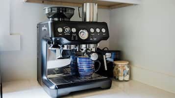 Une machine à expresso compacte dotée d’un écran numérique, d’un embout pour faire mousser le lait et d’une verseuse à café.