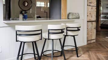 Une cuisine avec un plan de travail blanc, trois tabourets de bar et un plancher en bois.