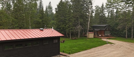 A cabin with a red roof, a deck, and a gravel driveway.