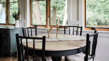 Une table à manger avec des chaises, un vase avec des bougies et une vue sur la verdure à travers de grandes fenêtres.