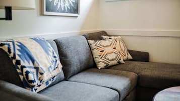 Un sofá gris con almohadones estampados y un cuadro en la pared.