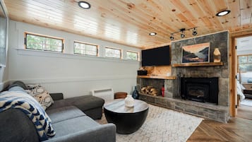 Een moderne woonkamer met een stenen openhaard, een grijze bank en een ronde salontafel.