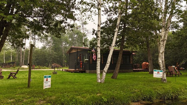 A rustic cabin with a porch, surrounded by trees, and signs indicating availability for rent.