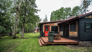 Een chalet met terras, omgeven door bomen en een klein zitgedeelte buiten.