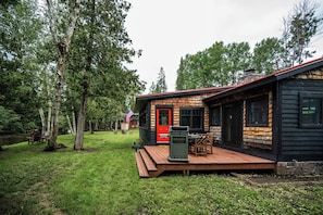 A cabin with a deck, surrounded by trees, and a small outdoor seating area.