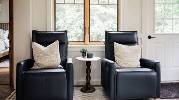 Two black leather chairs with matching cushions, a small round table with a plant and a mug, and a window with a view of trees.